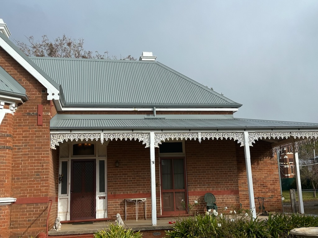 Heritage brick home with new grey corrugated roof and verandah above white iron lacework
